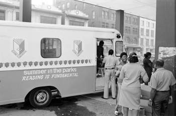 A line of people stands outside of a van, labeled "Summer in the Parks Reading is Fundamental."
