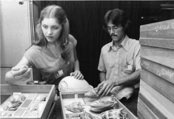 A woman and man reach in storage box cabinets that store shells. Both are wearing badges.