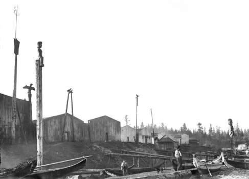 Shore lined with wooden houses, totem poles, and canoes.