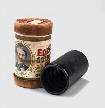 Upright cardboard tube with a label sitting next to a wax cylinder lying on its side.