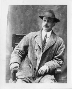 Black-and-white photograph of a man wearing a hat and coat sitting in a chair.