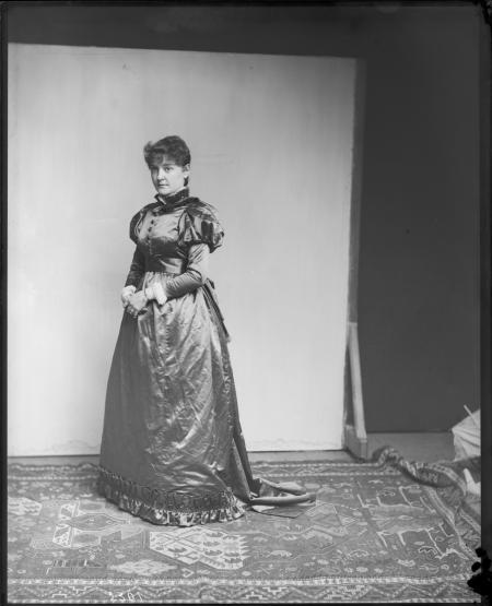 Portrait of woman, standing in front of a backdrop, wearing a long dress with large sleeves.