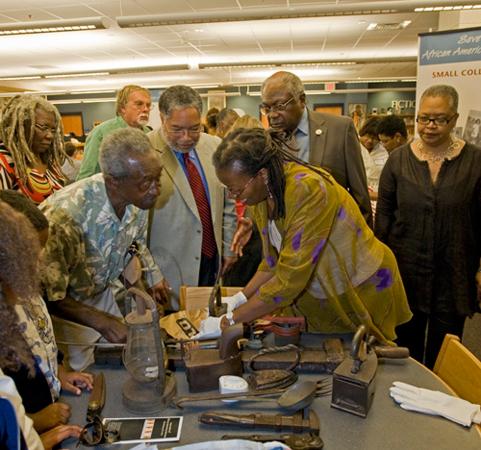 A group of people stand around objects in a table.