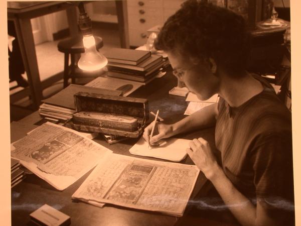 A woman sits at a table and takes notes as she analyzes an old text. 