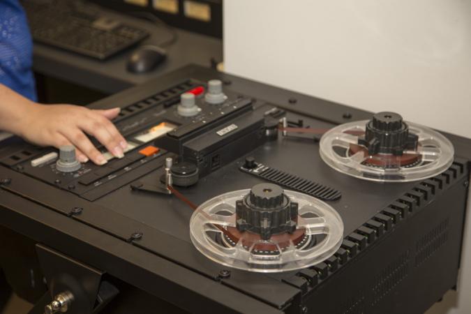 Kira Sobers works on an audio reel-to-reel tape recorder. It has two tape wheels and many buttons. 