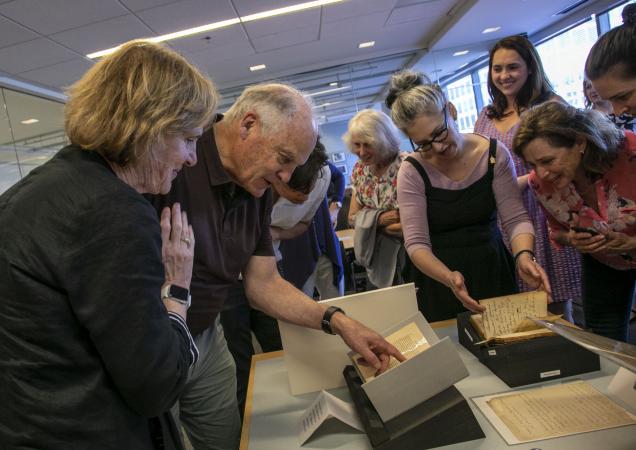 Men and women gather around a table of documents. People point to the documents.