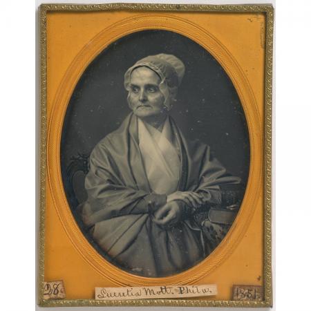 Portrait of a woman sitting. She is wearing a bonnet. The image is framed in an orange oval inside a