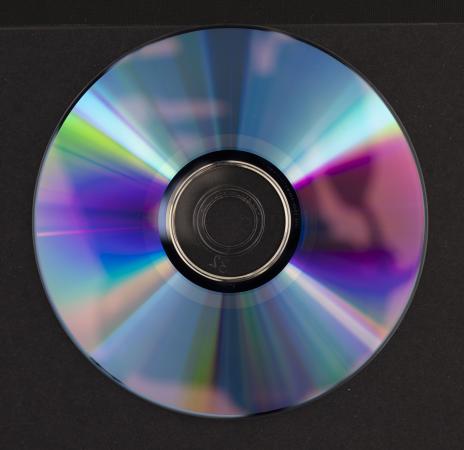 The iridescent reverse side of a DVD has an amorphous shadow that is a reflection from the camera.