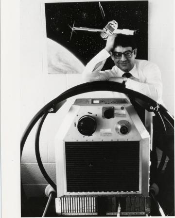 A man leans against a machine. A poster of space is in the background.