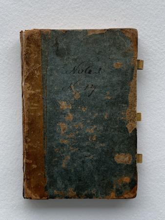 View of a leather-bound book cover with three loop holes at the edge. The cover is damaged and "note