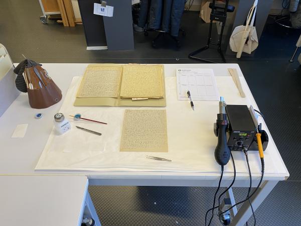 The damaged papers are on a desk next to conservation tools. 