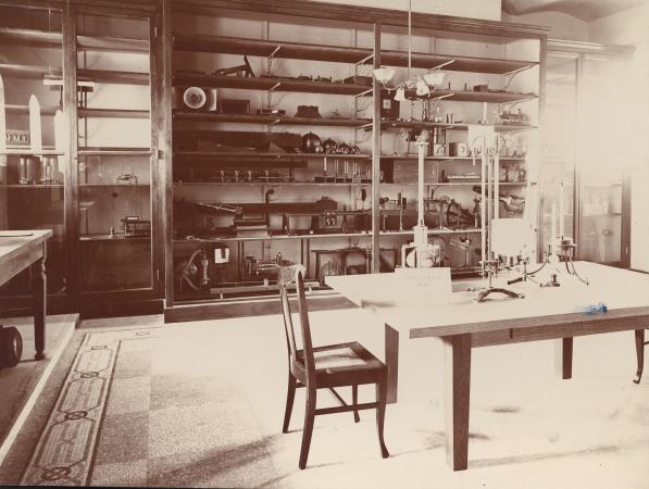 Faded photograph of a room with cluttered shelves and a work table.