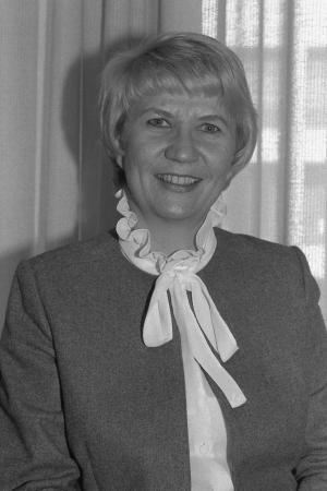 Portrait photograph of a white woman with short hair and a long, white neck scarf.