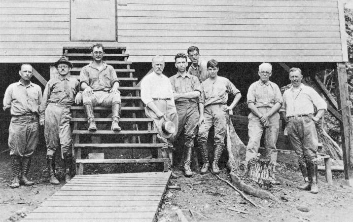 A group of nine men stand outside a structure on Barro Colorado Island. 