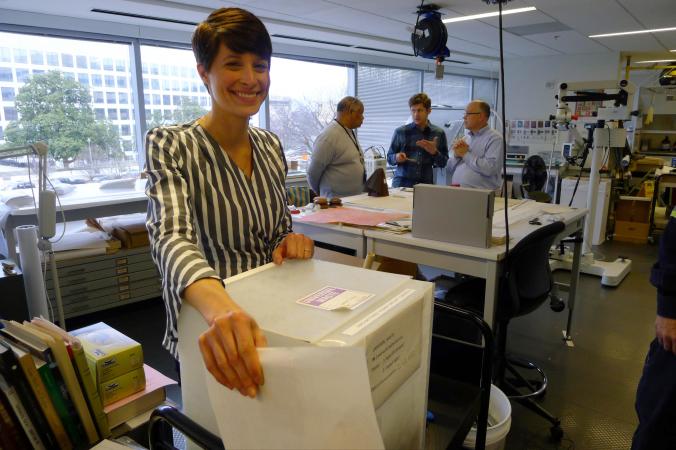 Alison smiles toward the camera and holds up a box labeled 