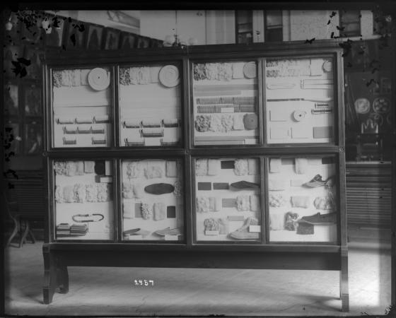 Textiles and single shoes are displayed in 8 sections in a mahogany case. 