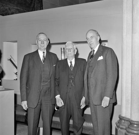 Three men in suits stand in a room.