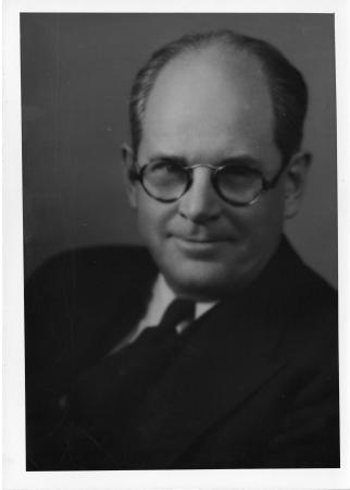 Portrait of Darling. He is wearing a suit and tie and thick, round glasses.