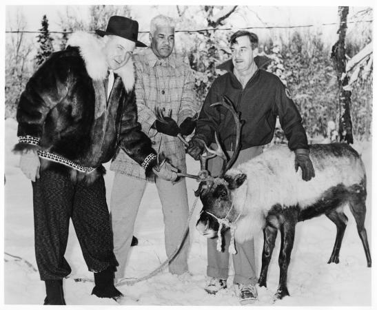 Three men stand in the snow with a reindeer. 