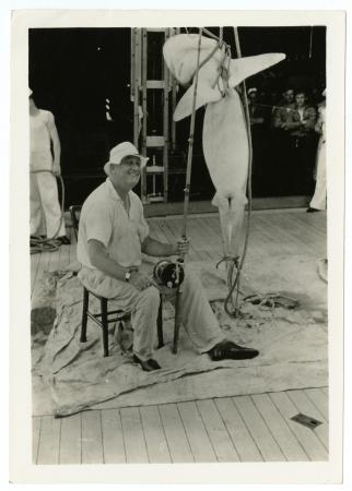 President Roosevelt sitting on a stool, leisurely dressed holding a fishing rod next to his large ca