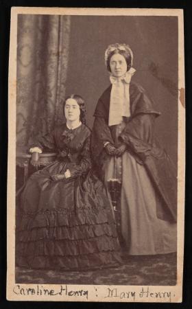 Caroline Henry is seated and Mary Henry stands behind her. Both women are wearing long dresses and n