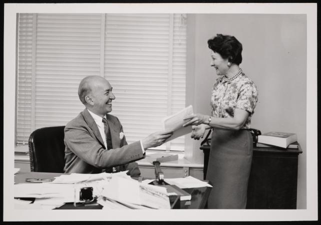 Portrait of Secretary S. Dillon Ripley with a woman in an office. Ripley is seated at a desk.