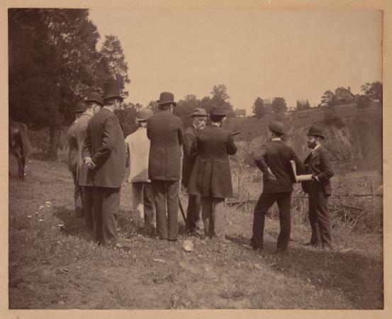 Men wearing suits stand in an open field. 