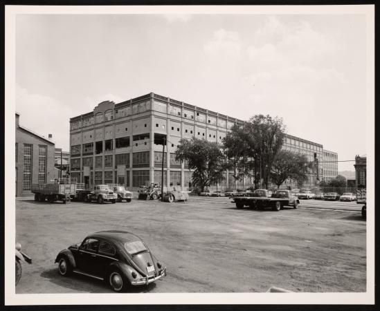 Exterior view of a building. 1960s cars are parked in the streets. 