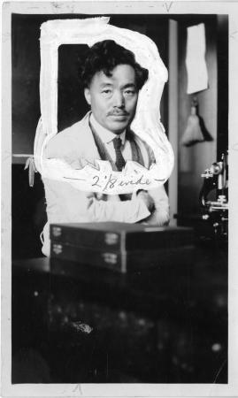 Image of a person wearing a lab coat sitting at a desk. The photograph was edited, so there is a whi