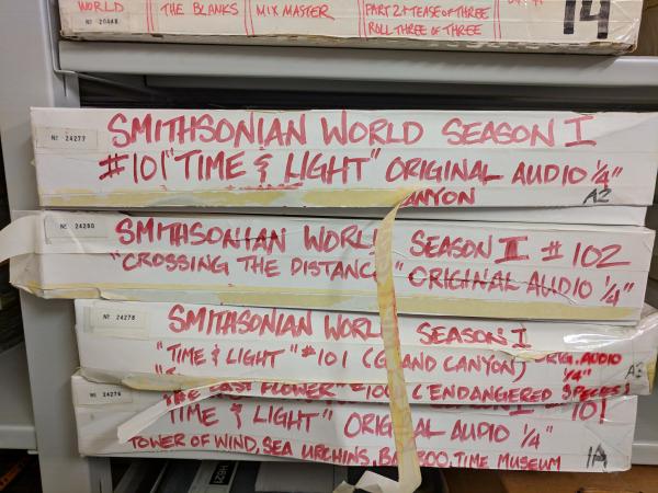 Long, thin cardboard boxes labeled "Smithsonian World" with various episode titles. The boxes are st