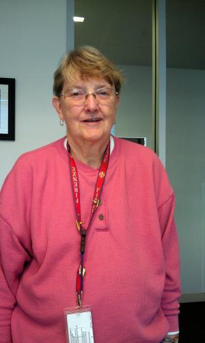 Color portrait of Zoe Martindale standing, wearing a pink shirt and lanyard around her neck with a I